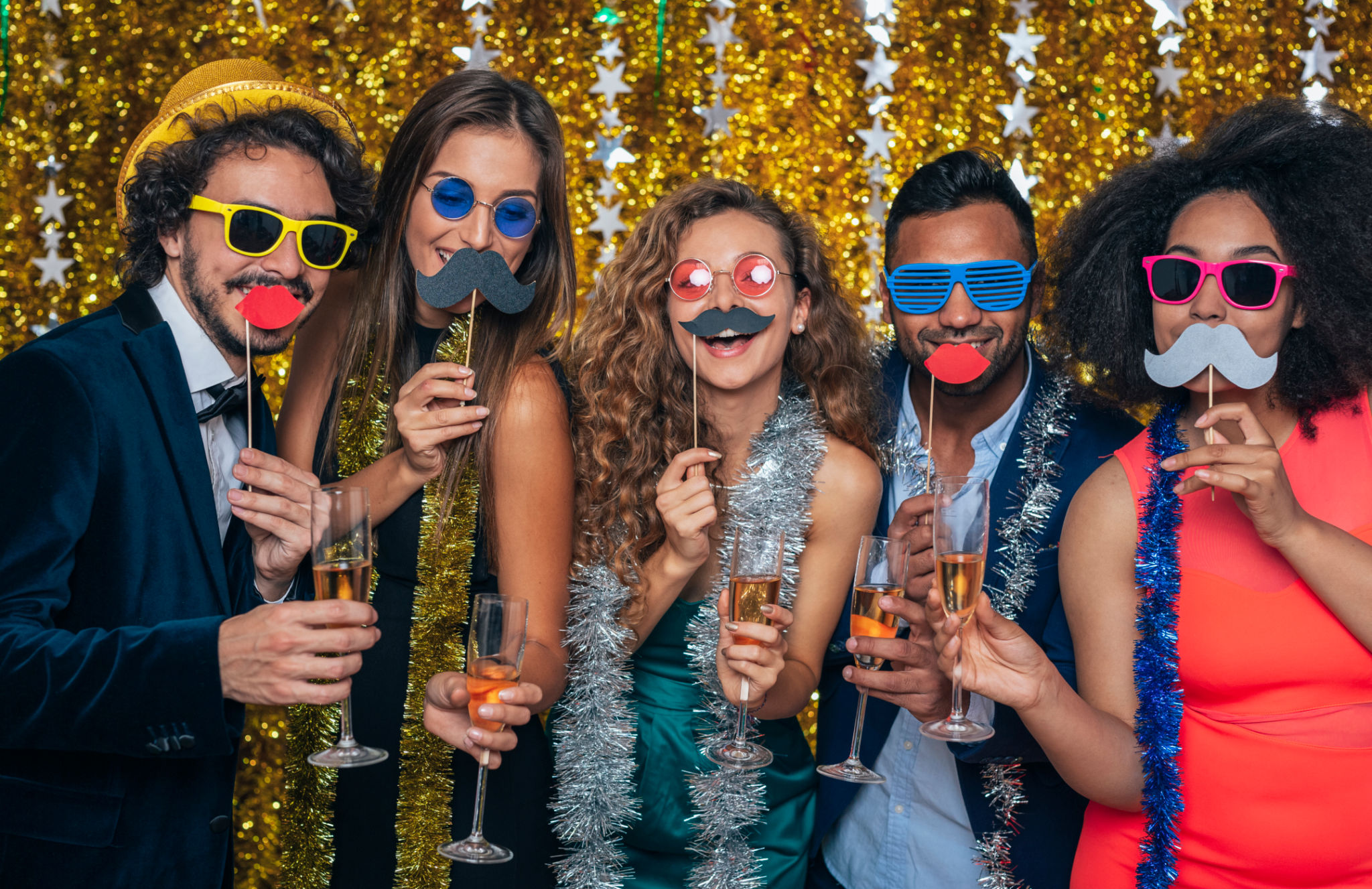 Portrait of Group Of Friends Celebrating At New Year Party Together holding photo booth fake props as moustaches, glasses and kiss lips and posing at camera